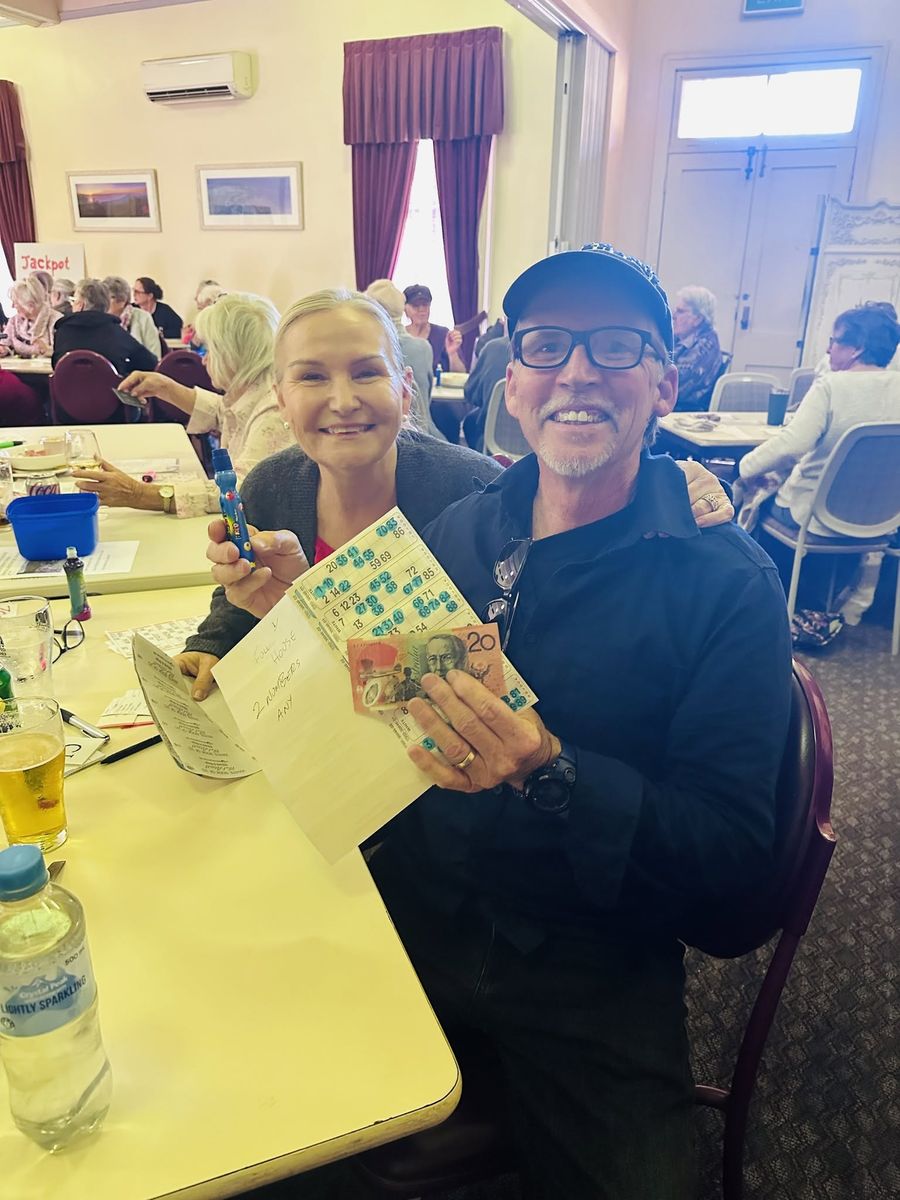 A smiling couple holding a bingo card and a twenty dollar note